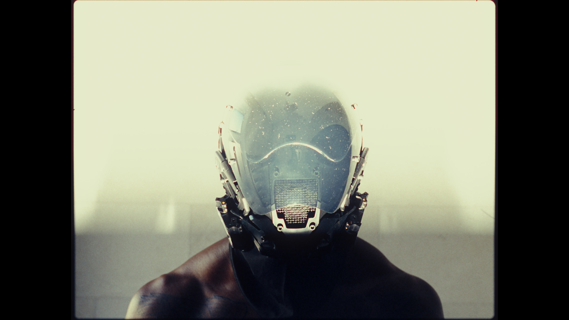 A figure in a full-face helmet, front on, in bright haze; a 4:3 frame through S444 Film Lab: Vision3 250D negative, 2383 print